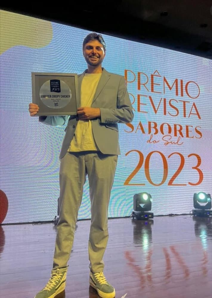 Luis Henrique Dobrovolski Lopes sorrindo no palco, segurando um prêmio