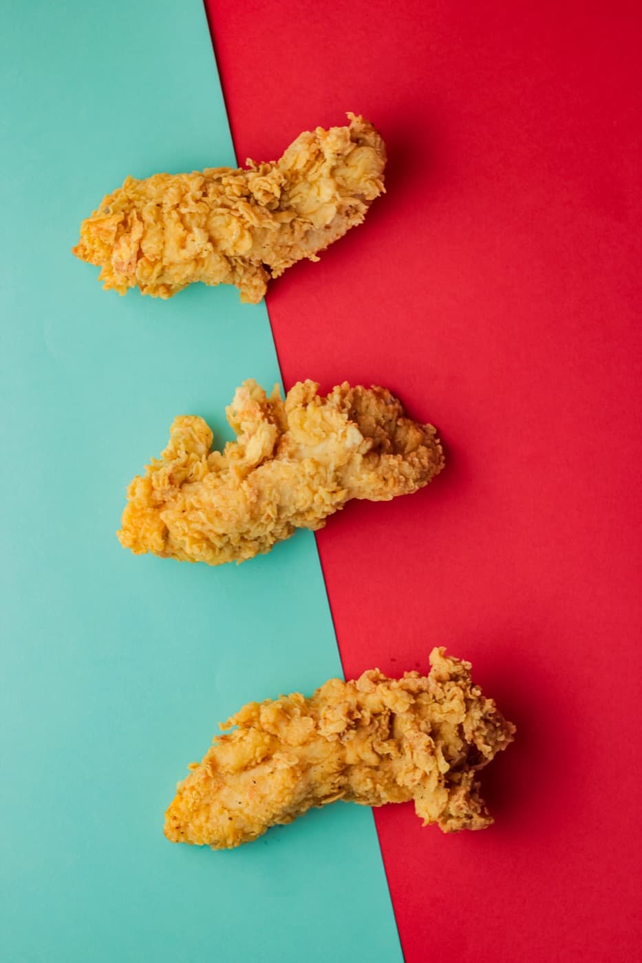 Tiras de frango frito sobre fundo vermelho e verde-água